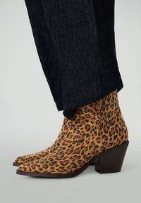 Bottines à imprimé léopard en suède texturé avec un bout pointu et un talon carré marron, associées à un pantalon en denim foncé.