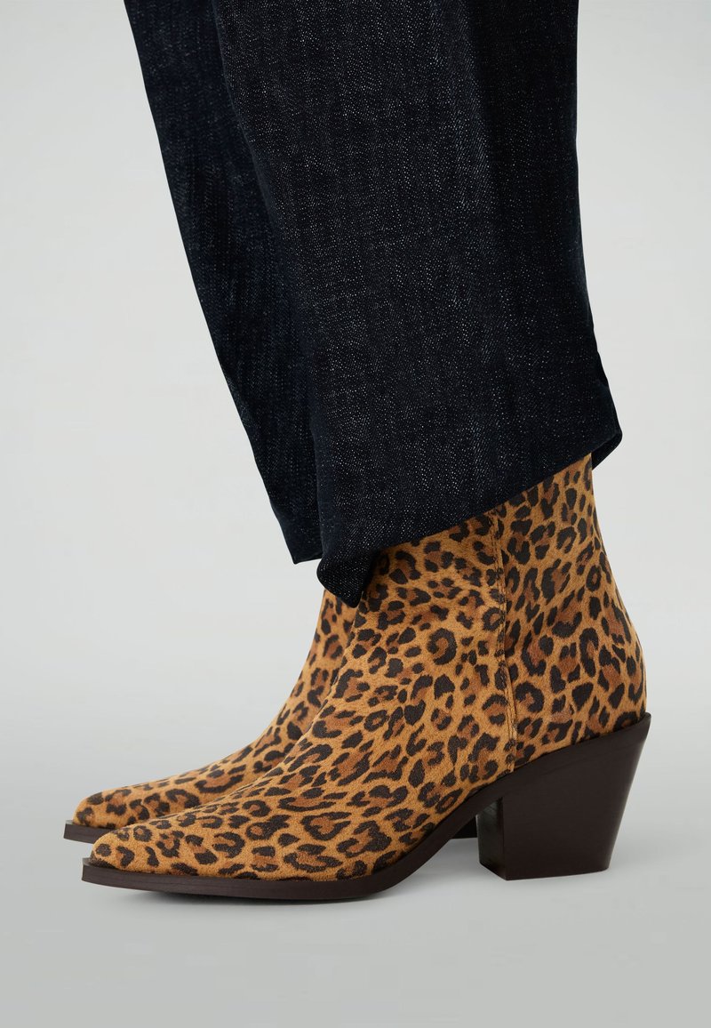 Bottines à imprimé léopard en suède texturé avec un bout pointu et un talon carré marron, associées à un pantalon en denim foncé.