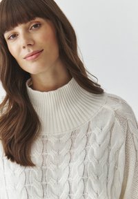 Maglione crema a trecce con colletto alto a coste, caratterizzato da una vestibilità ampia e motivi testurizzati su tutto il tessuto.