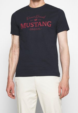 Marineblaue Baumwoll-T-Shirt mit Rundhalsausschnitt. Mit rotem Grafiktext "Denim Brand MUSTANG ORIGINAL" auf der Brust. Kurze Ärmel, normale Passform.