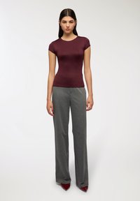 Top aderente bordeaux con maniche corte abbinato a pantaloni grigi a righe sottili in vita alta e tacchi a punta rossi. Texture liscia in tutto.