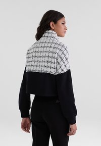 Cropped sweatshirt featuring a textured white and black checkered upper and solid black lower portion, with a high collar and loose sleeves.