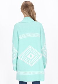 Minta zelena cardigan z belimi geometrijskimi vzorci, z ovratnikom in ohlapnim krojem. Tkanina se zdi mehka in pletena.