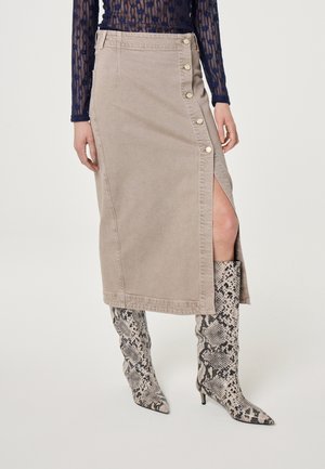 Beige midirok met knopen aan de zijkant en een split, gecombineerd met kniehoge, spits toelopende laarzen met slangenprint en een marineblauw kanten top.