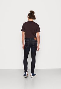 Kortärmad t-shirt i marinblått och rödrandig, kombinerad med mörka denim slim-fit jeans och blå högtoppssneakers med bruna och vita detaljer.