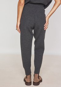 Joggers a maglia grigio carbone con vestibilità affusolata, vita elastica e polsini a coste, abbinati a stivaletti marroni su uno sfondo neutro.