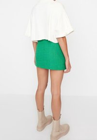 Haut blanc court, mini jupe texturée verte, et bottines beiges à semelle épaisse. La jupe a une silhouette ajustée.