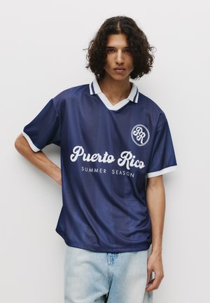 Námořnická modrá krátkosrstá dres s bílými akcenty, s nápisy "Puerto Rico" a "LETNÍ SEZONA" vytištěnými bílým písmem. Design s výstřihem do V.