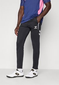 Mees, kes kannab musti Hummeli pükse, sinist ja roosat spordisärki, valgeid sokke ja valgeid Lotto spordijalatseid.