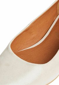 Chaussure plate blanche avec semelle intérieure en cuir brun clair lisse et bout arrondi, montrant la doublure intérieure et les détails de texture.