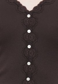 Brun ribbestrikket cardigan med en bølget blonder trim og fem hvite knapper, som fremhever detaljerte intrikate mønstre langs lukkingene.