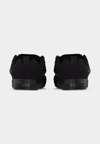 Ζευγάρι μαύρα αθλητικά Vans, εμφανιζόμενα από πίσω, με επενδεδυμένους γιακάδες και λογότυπα "Off The Wall" στις λαστιχένιες μεσαίες σόλες.