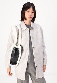 Giacca camicia in misto lana grigio chiaro con bottoni frontali, abbinata a un maglione grigio e pantaloni coordinati. Borsa foderata in pelliccia bianca e nera.