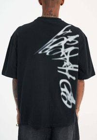 Camiseta de algodón negra de corte holgado con un diseño gráfico pintado con spray en blanco en la parte posterior, con un ajuste relajado y mangas cortas.