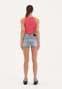 Top corto rosa y pantalones cortos de mezclilla azul deslavado con texto decorativo en la parte posterior. La modelo lleva zapatos de plataforma negros.