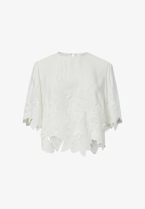 Valkoinen lyhythihainen pusero, jossa suuret kirjotut kukkakuviot ja siksakreunaiset helma- ja hiharesorit.