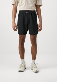 Black cotton shorts with an elastic waistband and a drawstring. The design includes side pockets and a small logo on the lower hem.
