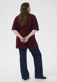 Suéter de punto burdeos con mangas cortas, combinado con jeans de campana azul oscuro y zapatos planos negros. Aberturas laterales visibles en el suéter.