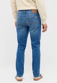 Blå denimjeans med rak passform, som har två bakfickor, en läderetikett i midjan och subtila blekningar längs benen.