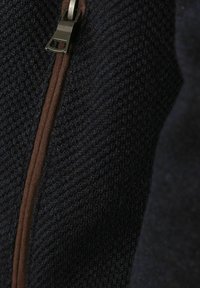 Dunkelblauer Strickstoff mit strukturierter Oberfläche, ausgestattet mit einem braunen Reißverschluss entlang der Naht für den Verschluss und als Detail.