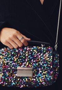 Juoda puošni rankinė su įvairiaspalvėmis blizgučiais ir sidabrine sagtimi. Rankinė turi petnešos grandinėlę ir stačiakampį formą.