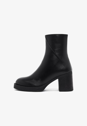 Bottine noire en cuir lisse avec une plateforme et un talon épais. Présente un design affiné et des détails cousus sur le côté.