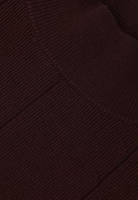 Burgundy kötött anyag bordázott textúrával. Ívelt nyakrész és ferde vonal jellemzi, amely strukturált megjelenést kölcsönöz.
