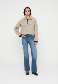 Μπεζ cropped σακάκι με δύο μπροστινές τσέπες, σε συνδυασμό με ανοιχτό μπλε φαρδιά τζιν και σκοτεινά παπούτσια. Απλός σχεδιασμός, λεία υφή.