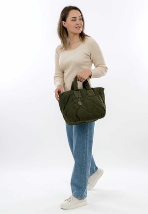 Quilted green tote bag with short handles, featuring a chain accent. Model wears a beige top and light blue jeans with white sneakers.
