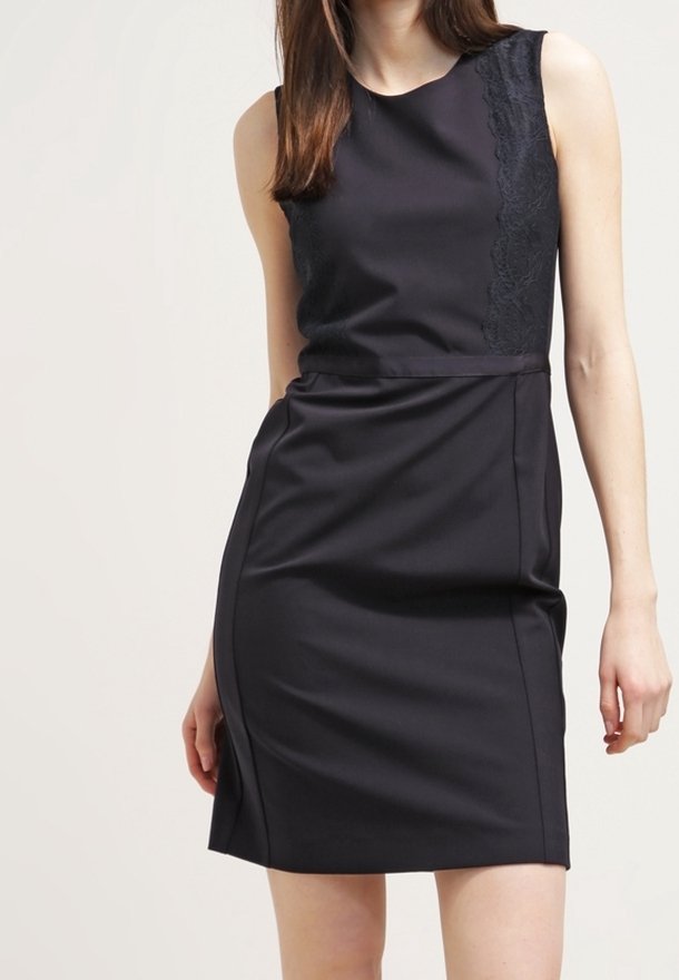 Svart ärmlös klänning med en figurnära silhuett. Har ett spetspanel på ena sidan och slät tyg. Knälång med en lätt lyster.