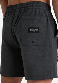 Pantaloni corti grigio scuro realizzati in un tessuto texturizzato, dotati di una vita elastica e di una tasca posteriore con un'etichetta nera.