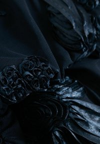 Tissu texturé sombre avec une rosette en ruban de satin complexe et des embellissements bouclés, créant un motif décoratif en couches et détaillé.