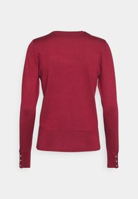 Pull en tricot bordeaux à manches longues, vu de dos, avec ourlet et poignets côtelés ornés de trois boutons argentés sur chaque manche.
