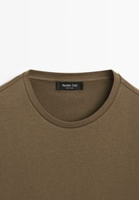 Olivengrøn t-shirt med rund hals, lavet af blødt stof. Enkel, glat tekstur med et mærke, der siger "Massimo Dutti."