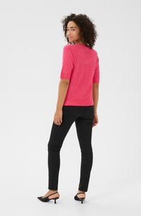 Pull en tricot rose vif à manches courtes avec une finition légèrement texturée, associé à un jean slim noir et des escarpins à talons slingback noirs.