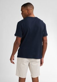 Námořnická modrá polo košile s krátkým rukávem, vroubkovaným límečkem a manžetami. Texturovaná tkanina, rovný lem a jemné kontrastní pruhy na manžetách.