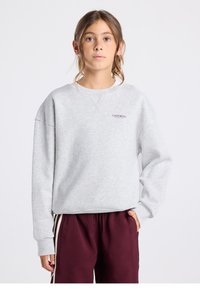 Suéter gris claro con cuello redondo y hombros caídos. Presenta un pequeño estampado "CALIFORNIA" en rojo. Combinado con pantalones burdeos.