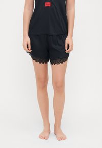 Zwarte shorts van rekbaar materiaal, met een gegolfde kanten zoom. Gecombineerd met een zwart topje met een klein rood logo aan de voorkant.
