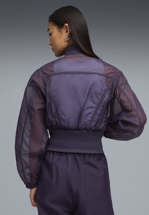 Violetti läpikuultava takki, jossa on korkea kaulus, topatut hihat ja resorivyötärö. Kangas on hieman kiiltävä ja siinä on teksturoitu kuvio.