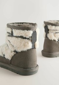 Gray boots with a soft, white fleece lining, featuring a textured surface, elastic straps, and a flat rubber sole.