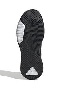 Semelle de chaussure de sport noire présentant un motif de relief texturé, avec une section en blanc et un detail de logo argenté.