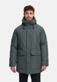 Grå vadderad parkas med huva, försedd med dragkedja framtill, två stora fickor fram och ett texturerat tyg med vattentät yta.