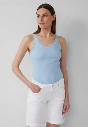 Hellblaues, geripptes Tanktop mit zarter Spitzenborte. Kombiniert mit weißen Shorts mit aufgerolltem Saum, die eine figurbetonte Silhouette zur Schau stellen.