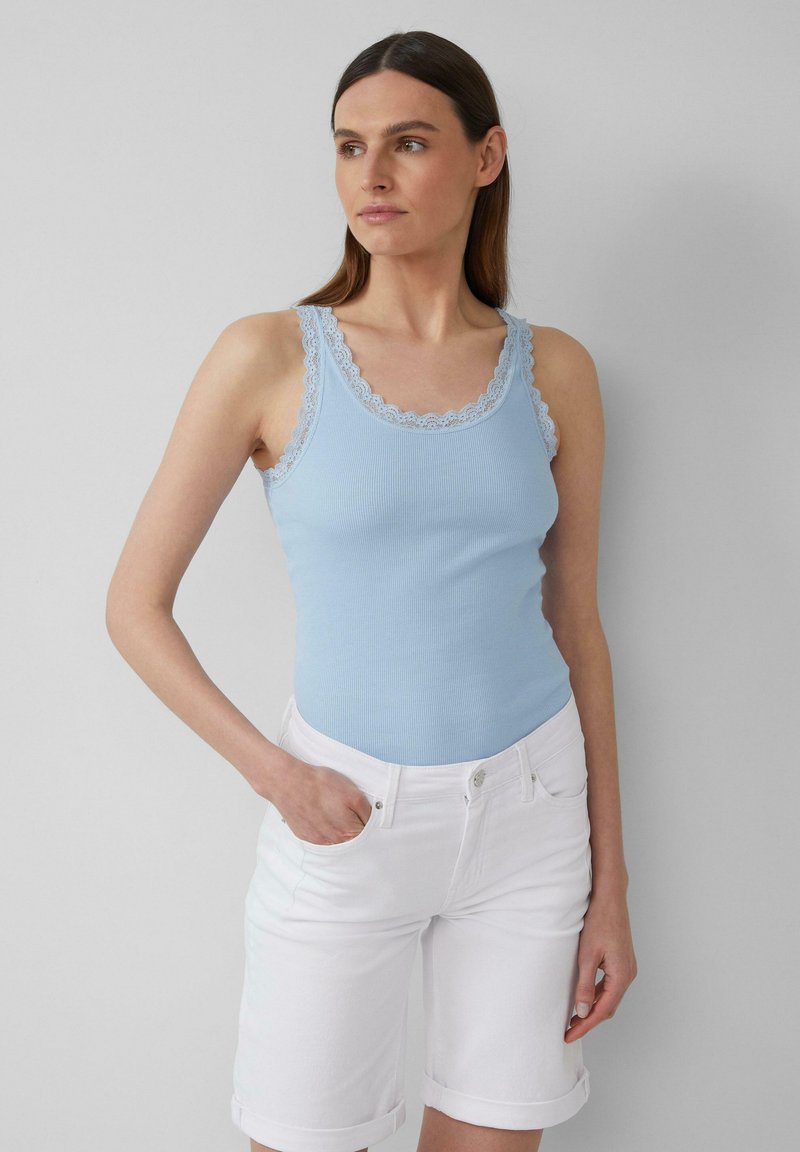 Lichtblauw geribbeld tanktop met verfijnde kantafwerking. Gecombineerd met witte shorts met omgeslagen zoom, die een aansprekende pasvorm benadrukken.