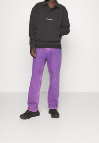Black long-sleeve polo shirt with logo, paired with light purple straight-leg jeans and black sneakers. The outfit features a relaxed fit.