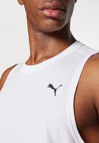 Chemise sans manches blanche en tissu lisse avec un logo Puma noir sur la partie gauche de la poitrine. Gros plan sur le col et les détails de l'épaule.