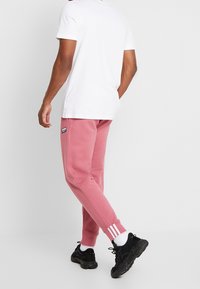 Light pink sweatshirt pants with ribbed cuffs and white triple stripes at the ankles, paired with a plain white t-shirt and black sneakers.