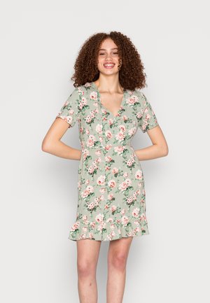 Vestido curto floral em verde claro, com decote em V, mangas curtas e bainha com babados, adornado com padrões de flores em rosa e branco.