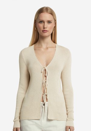 Beige stickad cardigan med djup V-ringning och snörning fram. Långa ärmar, texturerad tyg och en avslappnad passform. Subtil lyster och delad nederkant.