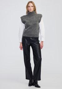 Szary wełniany sweter z golfem o oversize'owych ramionach, nałożony na białą koszulę, w połączeniu z czarnymi skórzanymi spodniami o szerokich nogawkach i botkami za kostkę.